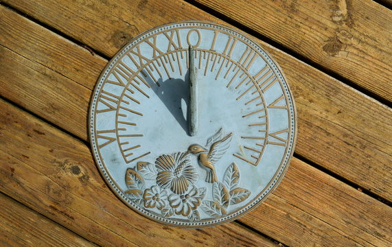 Horizontal sundial on a wooden background showing nine o'clock