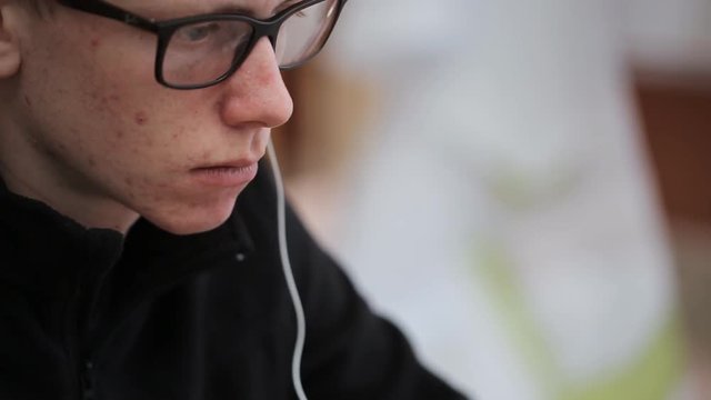 Young male student with glasses and pimples on face with headset.