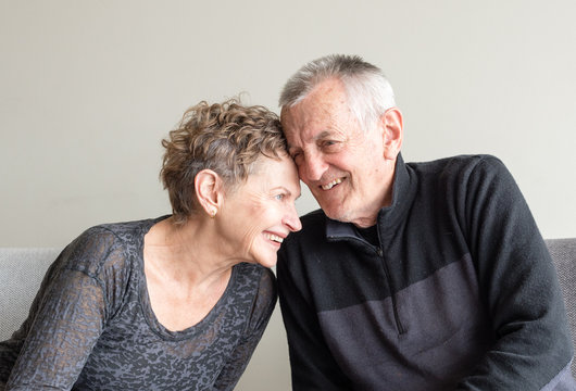 Older Couple In Black Clothing Leaning In With Heads Together Laughing (cropped)