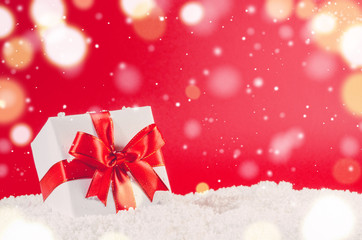 white decorative christmas gift box with ribbon on snow against red festive background