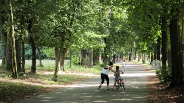 Woman teaching little girl biking in the cycleway inside the park in Monza, Italy. 4k