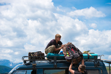 man gives another  a backpack on the roof of the car