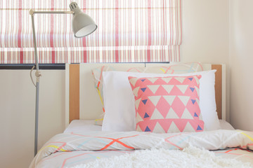 Coral pink triangle pattern pillow setting on bed with foldable reading lamp next to bed