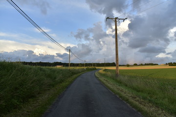 Fototapeta na wymiar Route de campagne sous la lumière du soir contrastant avec les nuages gris après le passage d'un front froid au Périgord Vert