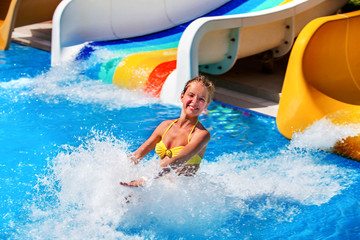 Child on water slide at water park . Child girl in water splashes.