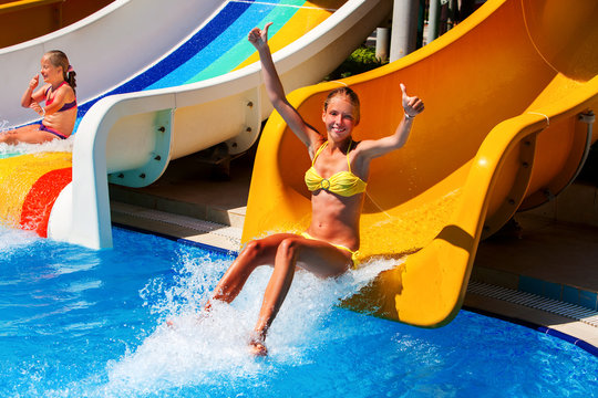 Child on water slide at water park show thumb up and jumb in water. .Summer outdoor water park .