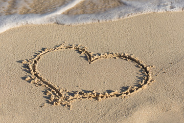 Shape of heart on sandy beach with wave's foam