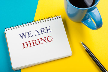 We are hiring. Office desk table with notepad, pencil and coffee cup. Top view.