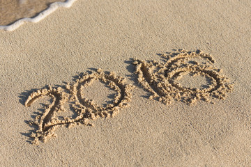Inscription 2016 on sandy beach with wave's foam