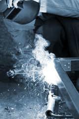 Worker in protective mask welding steel railings outdoors