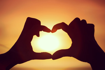 Silhouette of hand in heart shape with sun in the middle
