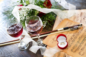 Gold ring, red rose, wine and violin on music notes 