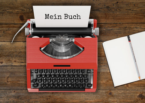 Schreibmaschine mit MEIN BUCH-Text und Notizbuch auf Holztisch 