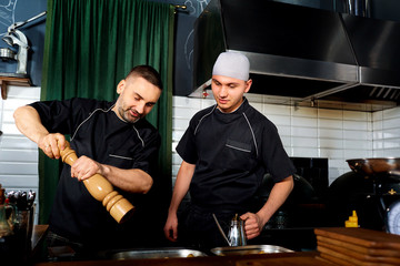 Fototapeta na wymiar Two chefs in a restaurant cook together. Cook adds seasoning to
