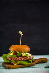 Tasty grilled tuna burger with lettuce and mayonnaise served on wooden table with copyspace