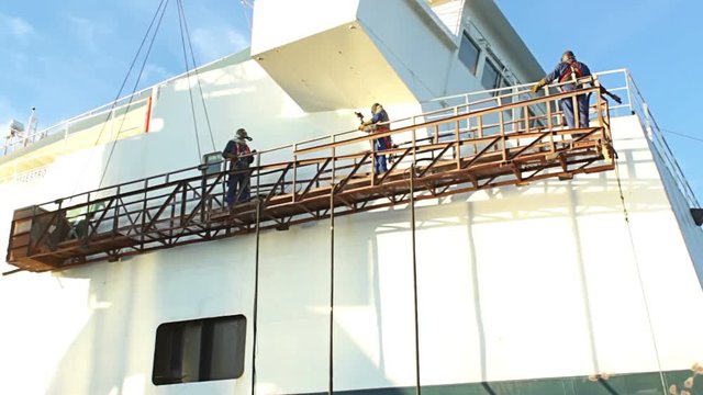 Shipyard Workers repairing and painting new layer of paint on modern ship