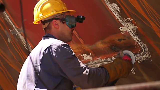 Workers polishing and welding during reparation of ship in shipyard with protective equipment