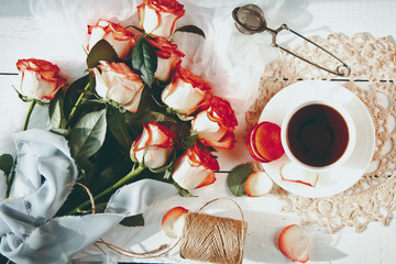 A beautiful bouquet of roses, tea Cup,with macaroons on  distressed white wood table. vintage style