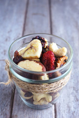 Close up of a jar of healthy mixed dried fruit and nuts on a wooden table.