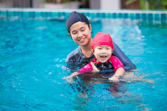 Young active mother having fun in a swimming pool with asian kid