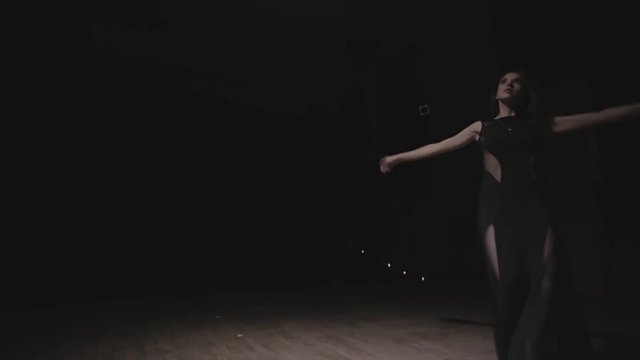 Woman in black dress is dancing on a dark stage under the spotlight