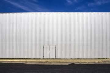 Fototapeta na wymiar Corrugated sheet metal wall with a door, the street shadows and blue sky. Outdoor. Industrial look. Digital background for photographers.