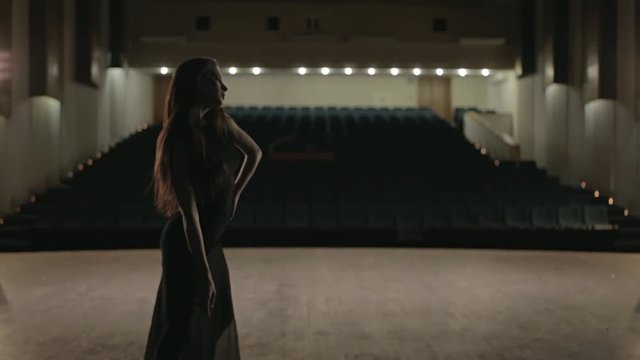 Woman in black dress is dancing on the stage in empty hall