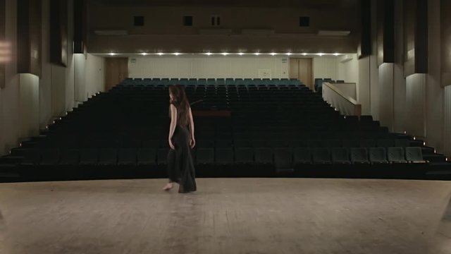 Woman in black dress is dancing on the stage in empty hall