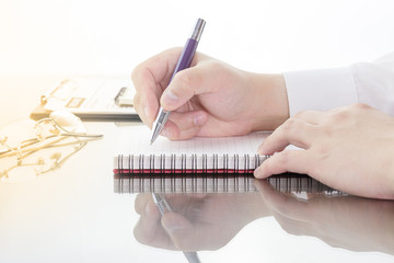 Businessman write a short note on opened notebook with pen and glasses.