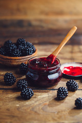 Fresh homemade blackberry jam in glass jar on a wooden background
