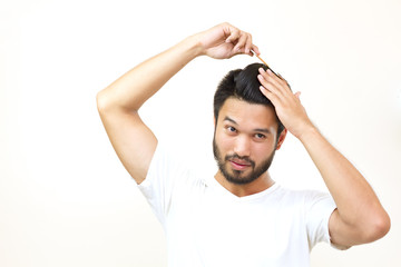 people concept - smiling young man brushing hair with comb on wh