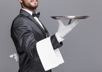Butler holding a silver tray on gray background