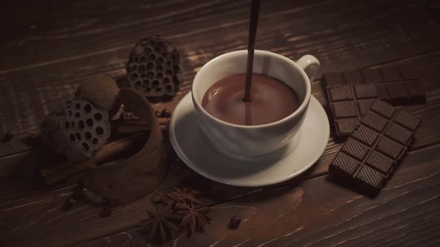 pouring hot chocolate with anise and cinnamon sticks on dark wooden table