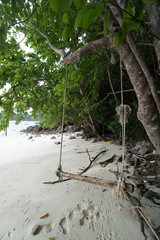 Swing hanging under the tree and footprints on a beach of tropical island in Thailand