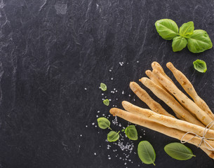 Bread sticks with salt and herbs on dark board, from overhead.