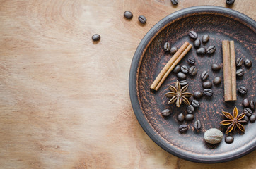 Coffee beans, cinnamon stick, star anise in a ceramic plate on a wooden background.
