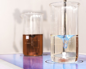 Glasses with chemical liquids are on a magnetic stirrer.