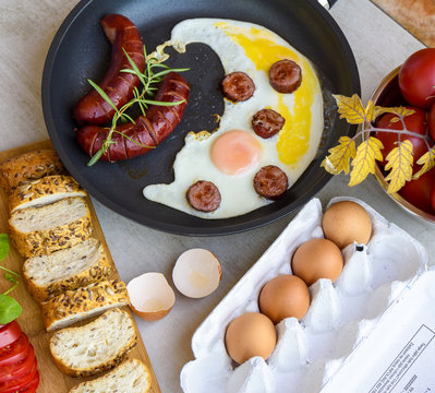 Fried sausages and eggs in a pan served with bread, tomatoes and egg shell, TOP VIEW