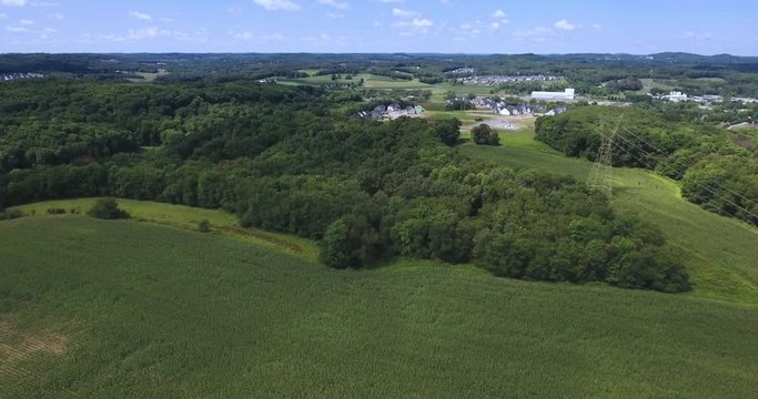 A high angle aerial view over corn fields and woods near a Western Pennsylvania farm.  	