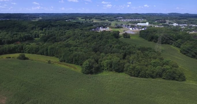 A high angle aerial view over corn fields and woods near a Western Pennsylvania farm.  	