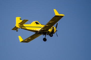 Fototapeta na wymiar Yellow Crop Dusting Plane Flying in a Blue Sky