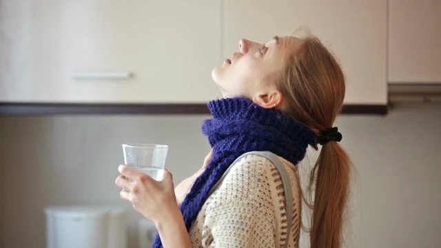 Girl with quinsy taking medicine and gargling throat in kitchen
