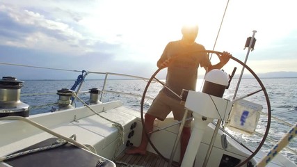 man on steering wheel navigating sail boat - Powered by Adobe