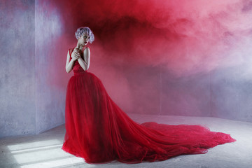 Fashion photo of young magnificent woman in red dress. Textured background, smoke