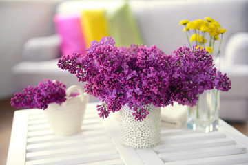 Lilac bouquets in ceramic vases on white wooden table