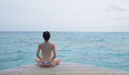 Fototapeta na wymiar woman with yoga pose in front of a clear aqua ocean in Maldives