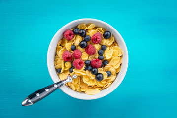 Cornflakes cereal with raspberries and bilberries and black currant in a white bowl on the blue...