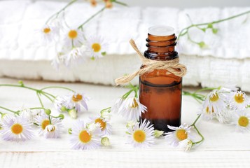 Essential oil, aroma dropper bottle decorated with twine, flowers, white bathroom terry towel. 