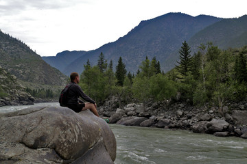 man sitting on a large rock over mountain river