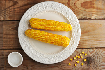 two corn cobs on a plate with salt.